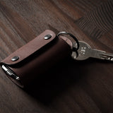 Dark brown leather key holder with keyring, key and car key fob on wood background