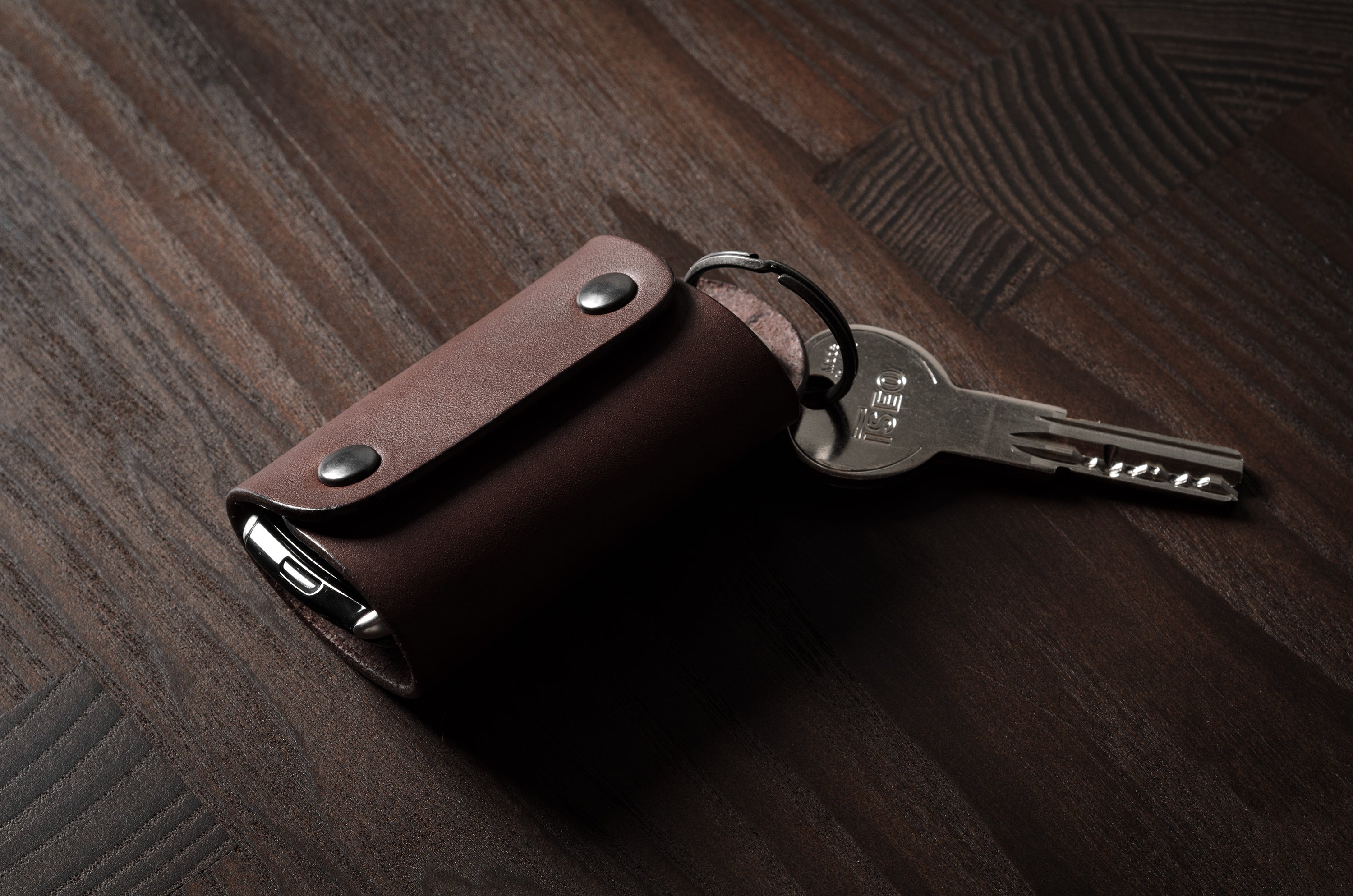 Dark brown leather key holder with keyring, key and car key fob on wood background