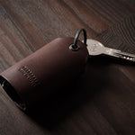 Dark brown leather key holder with keyring, key and car key fob on wood background