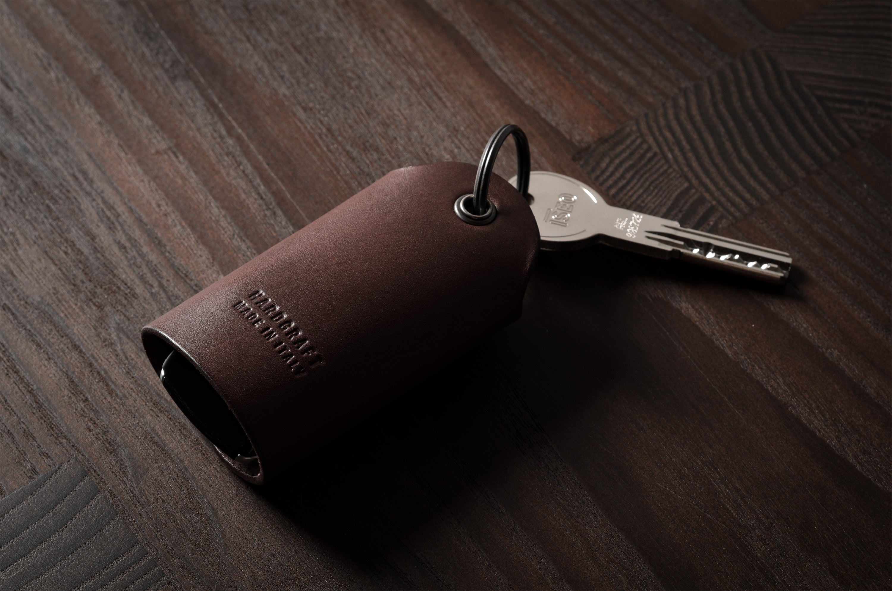 Dark brown leather key holder with keyring, key and car key fob on wood background