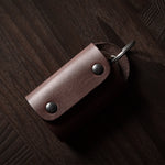 Dark brown leather key holder with keyring and key on wood background