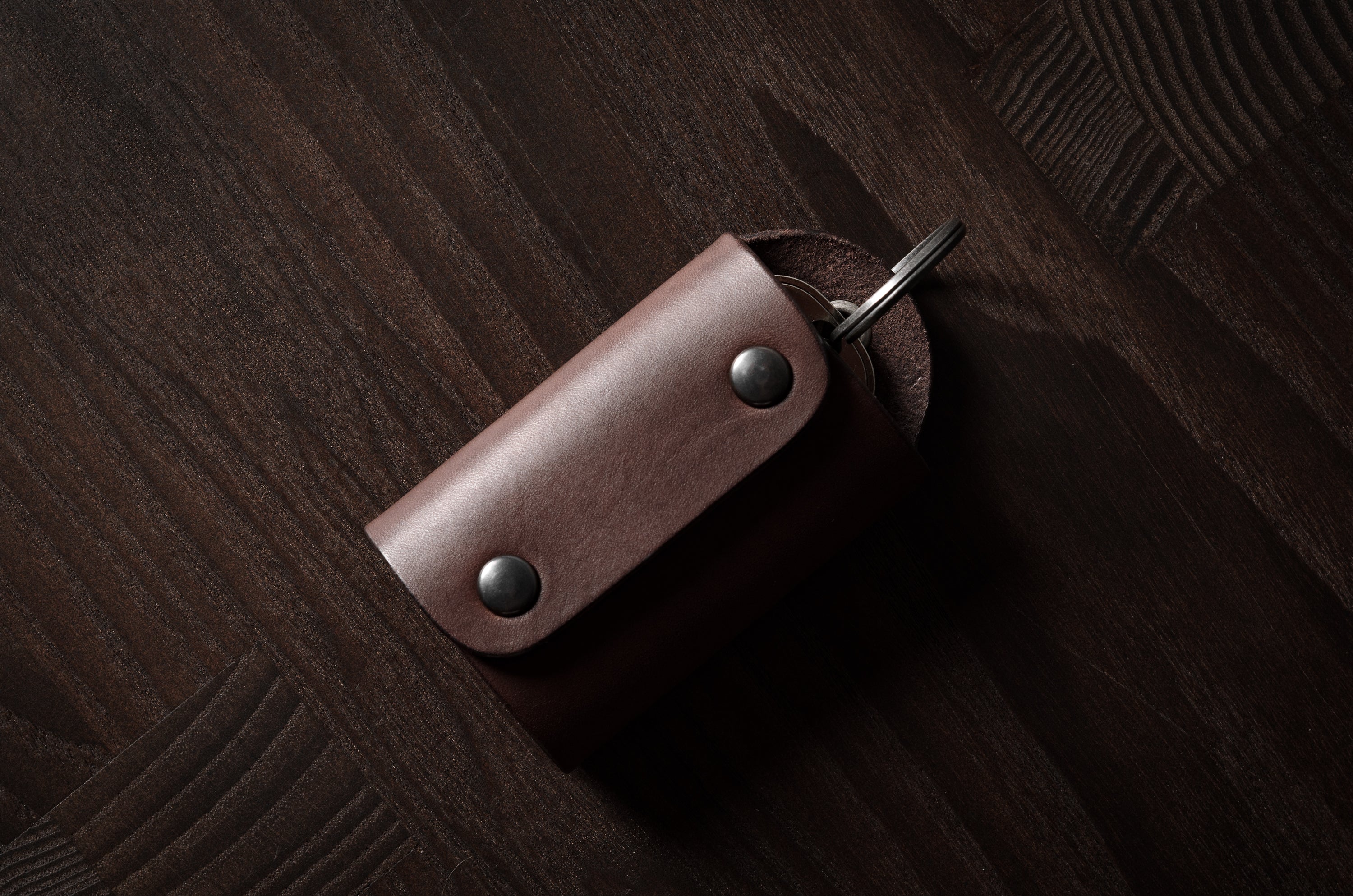 Dark brown leather key holder with keyring and key on wood background