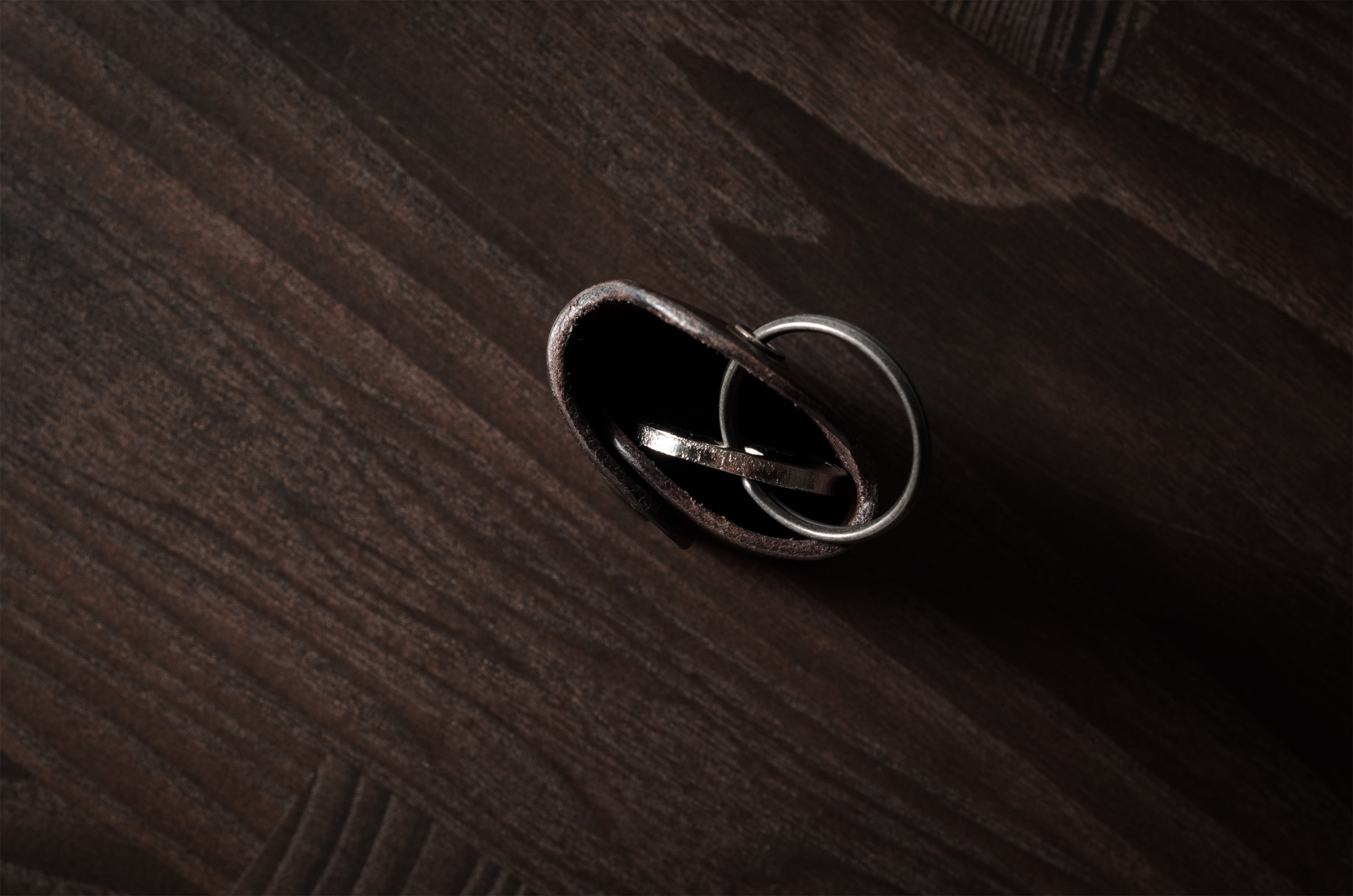 Dark brown leather key holder with keyring and key on wood background