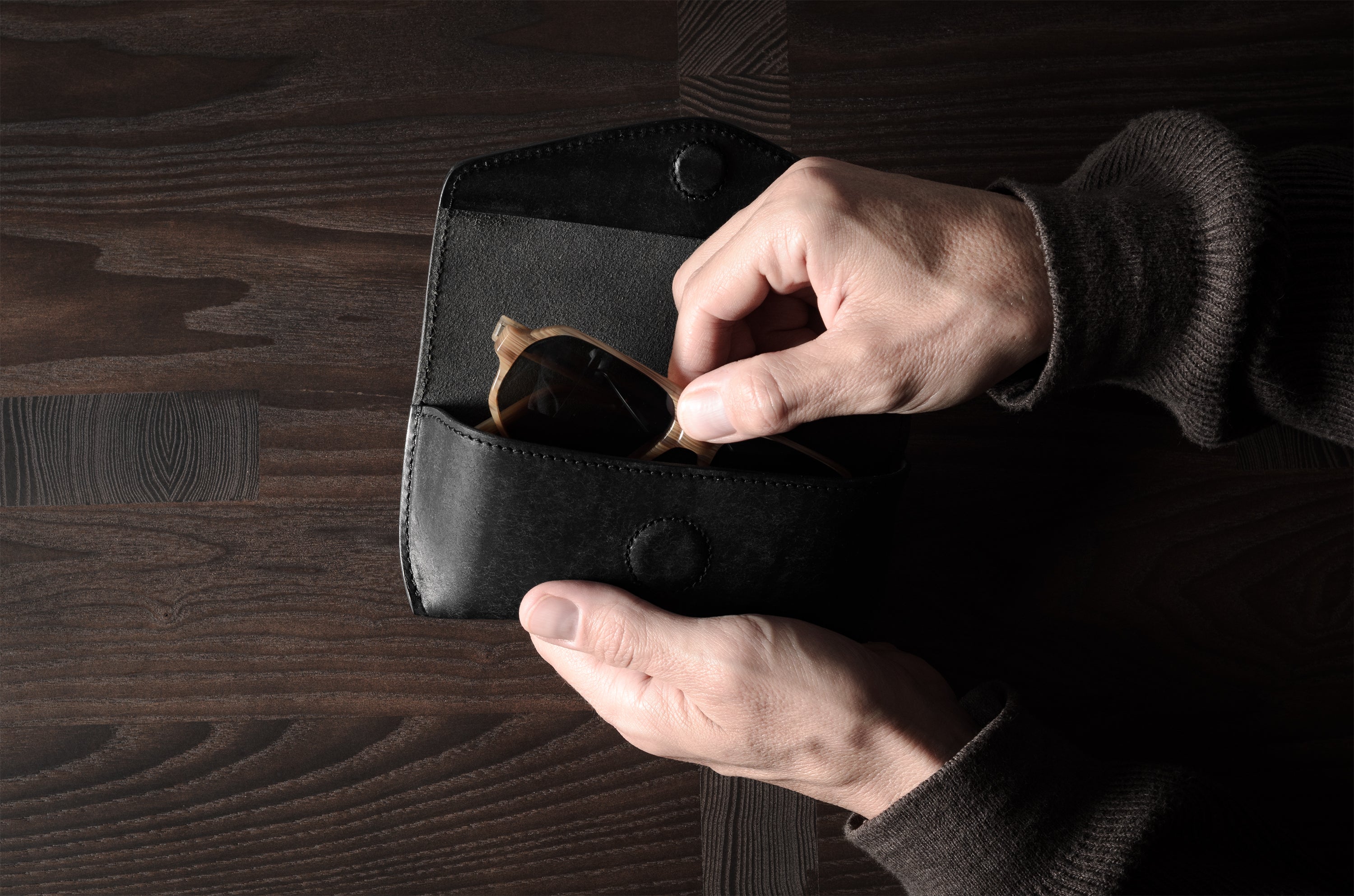 Black leather glasses case with sunglasses in hand