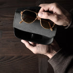 Black leather glasses case with sunglasses in hand