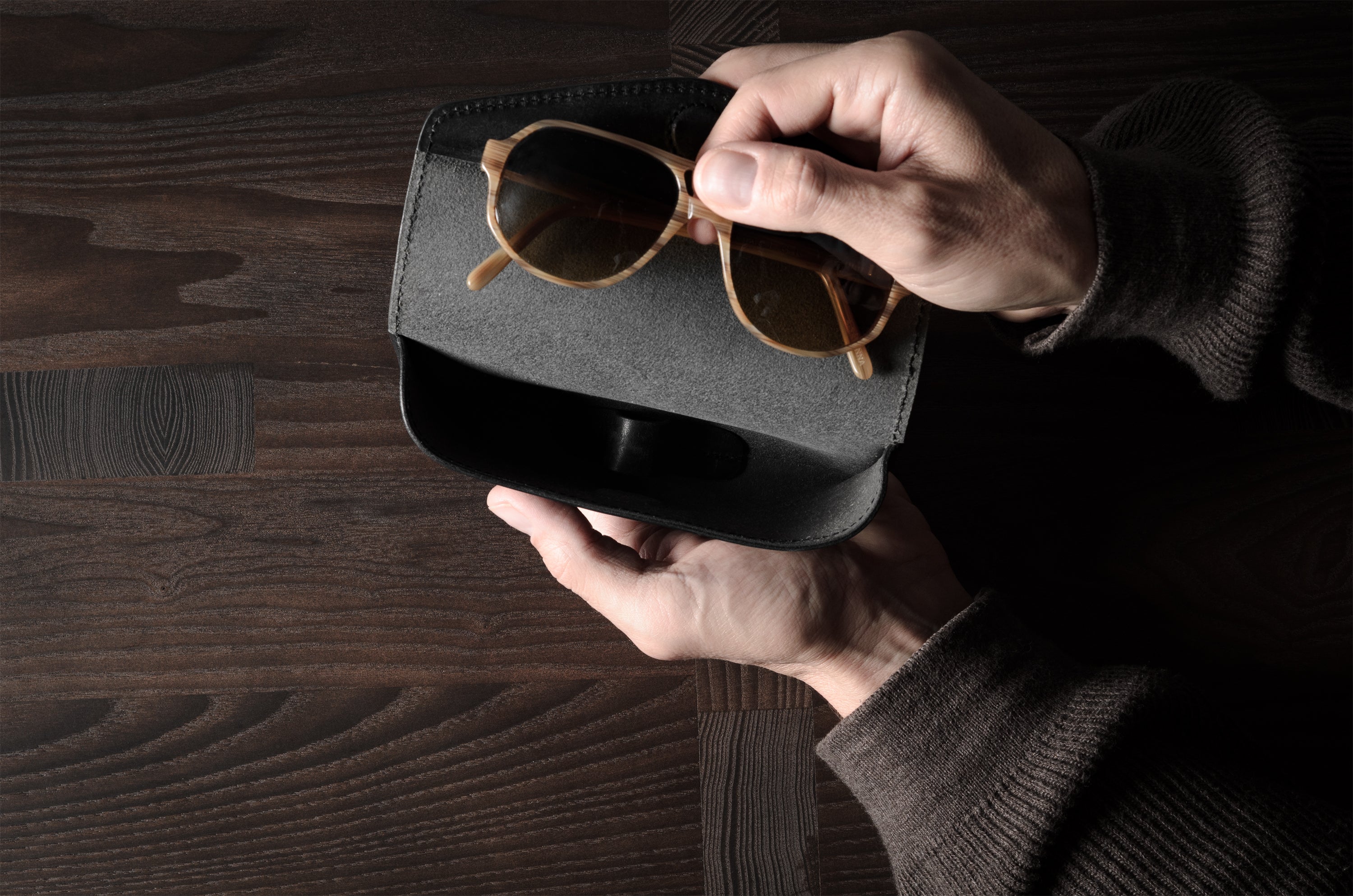 Black leather glasses case with sunglasses in hand