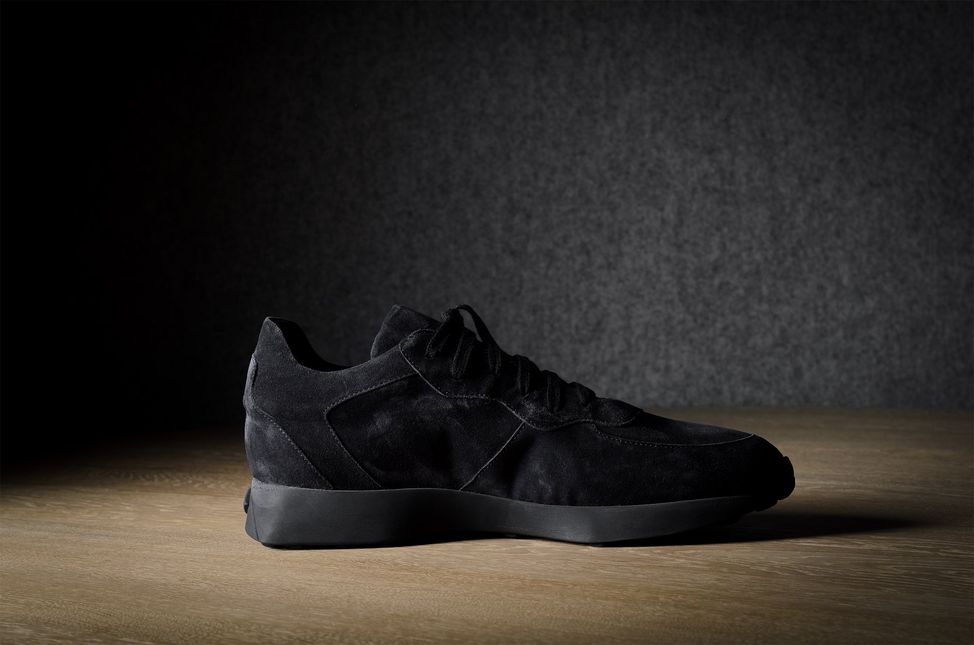 Black suede sneakers on a grey and brown wood background.