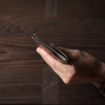 Person holding a brown leather passport case on a wooden surface