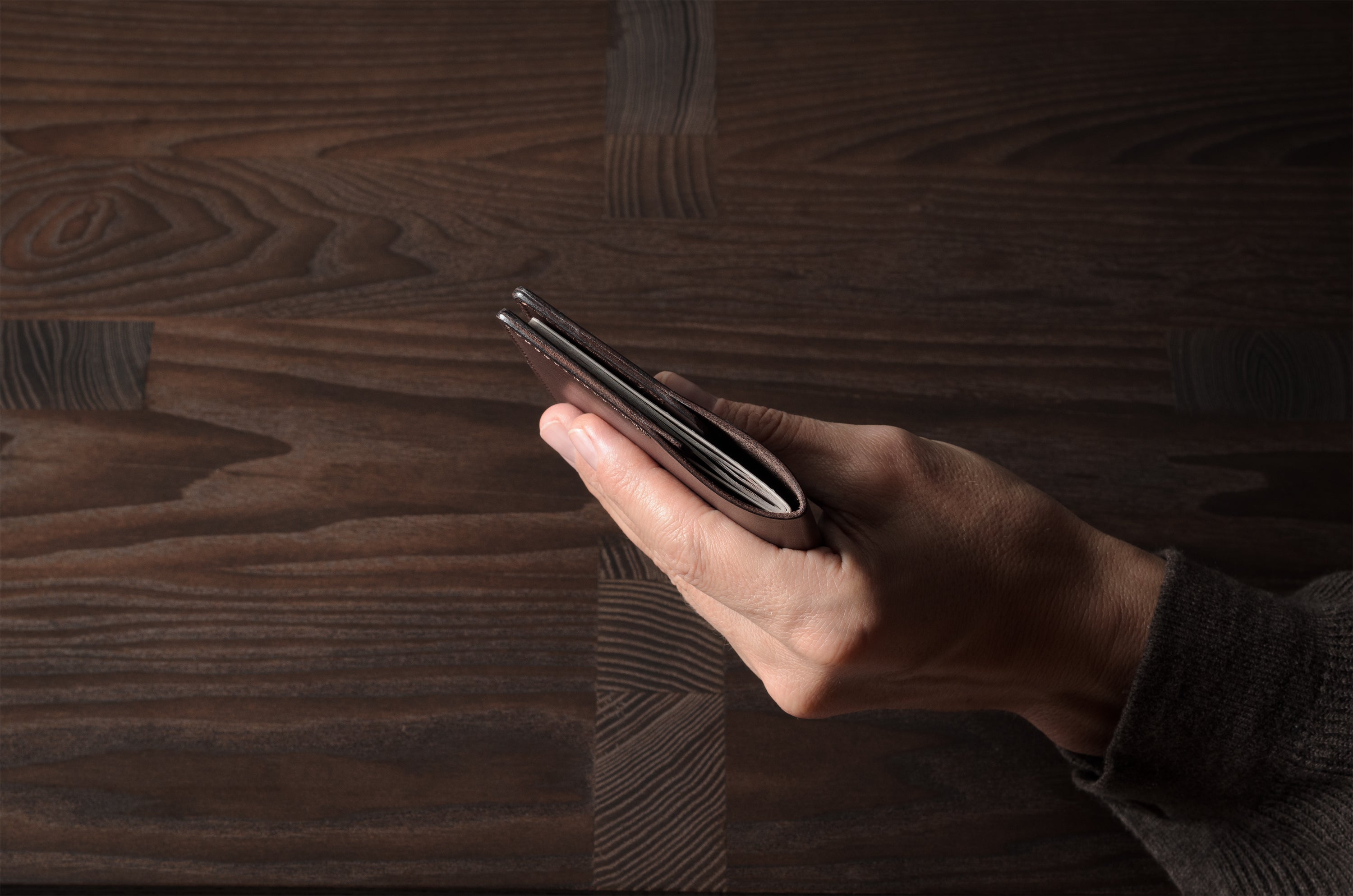 Person holding a brown leather passport case on a wooden surface