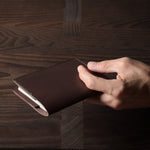 Person holding a brown leather passport case on a wooden surface