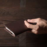 Person holding a brown leather passport case on a wooden surface