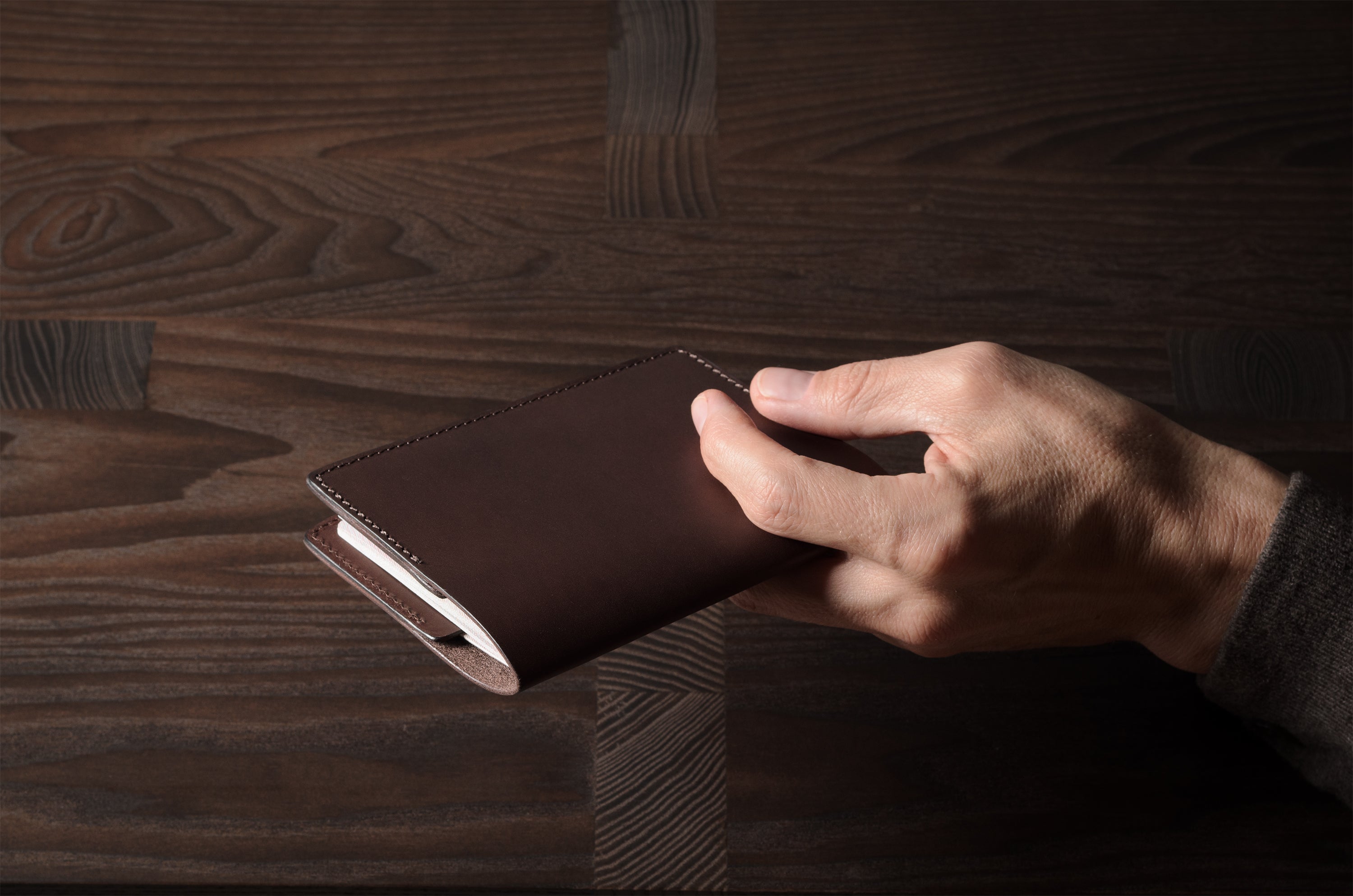 Person holding a brown leather passport case on a wooden surface