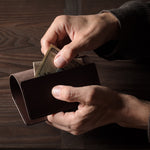 Person holding a brown leather passport case on a wooden surface