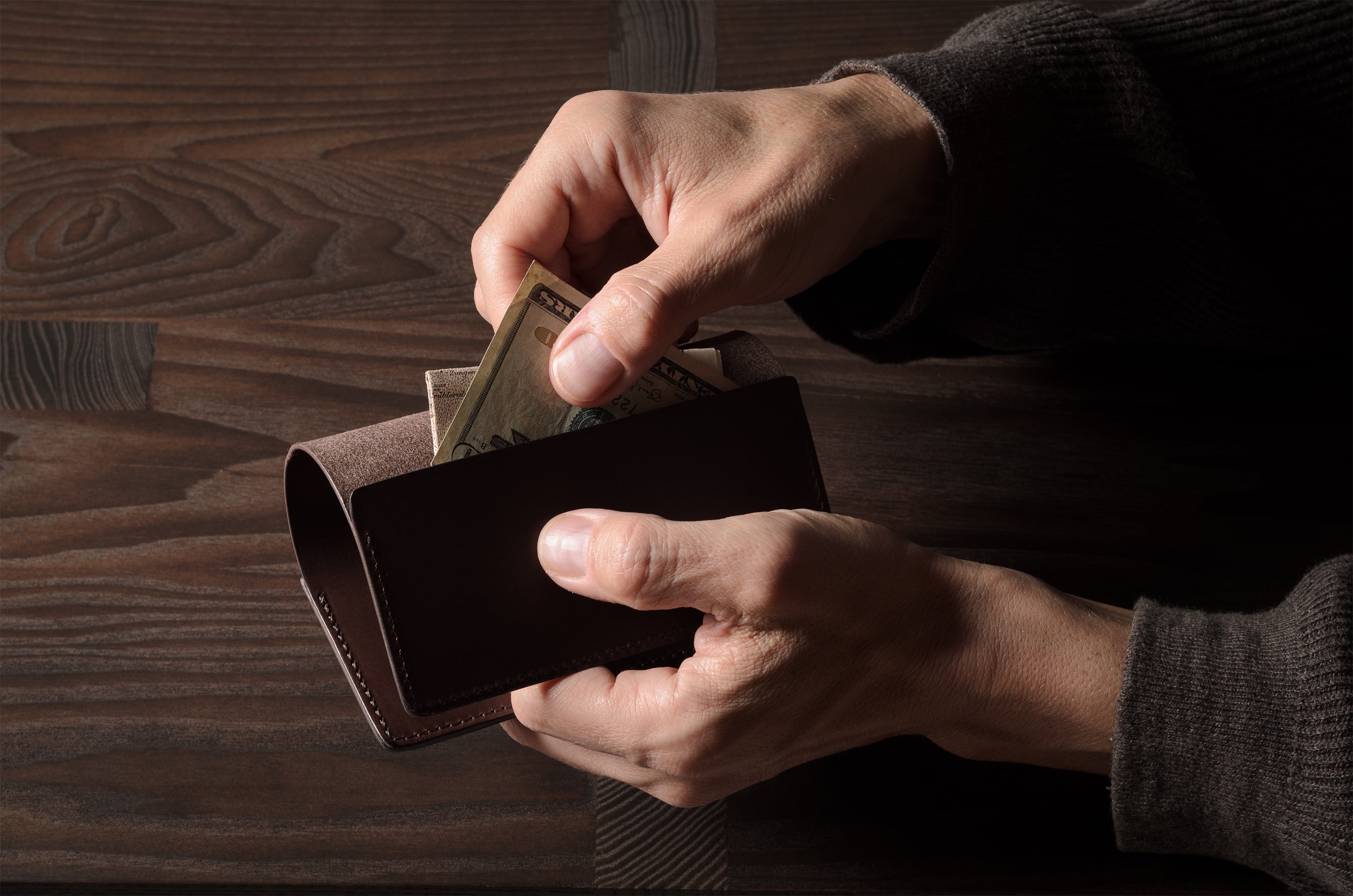 Person holding a brown leather passport case on a wooden surface