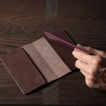 Person holding a brown leather passport case on a wooden surface