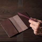 Person holding a brown leather passport case on a wooden surface