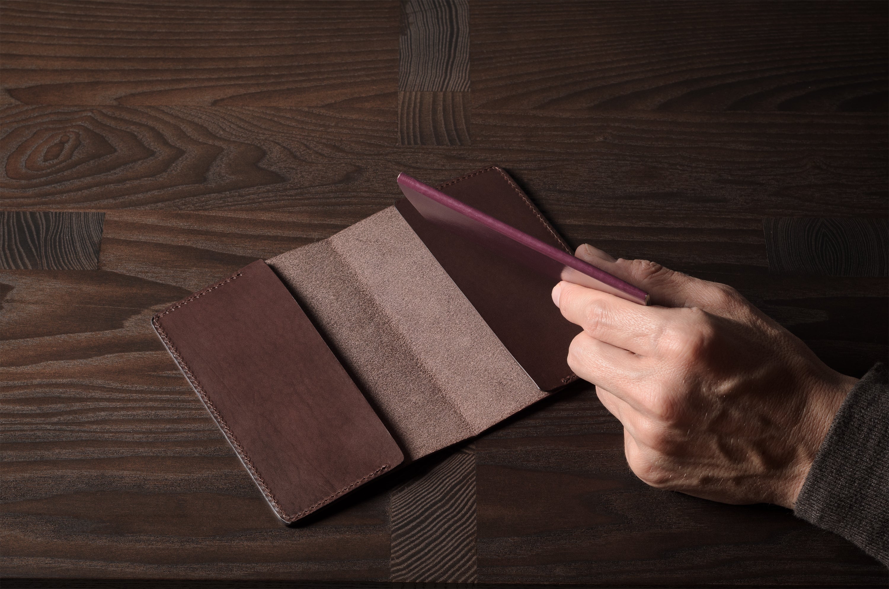 Person holding a brown leather passport case on a wooden surface