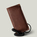 A brown textured leather iPhone 18 Pro case with a black coiled cord, shown standing upright on a light gray background.