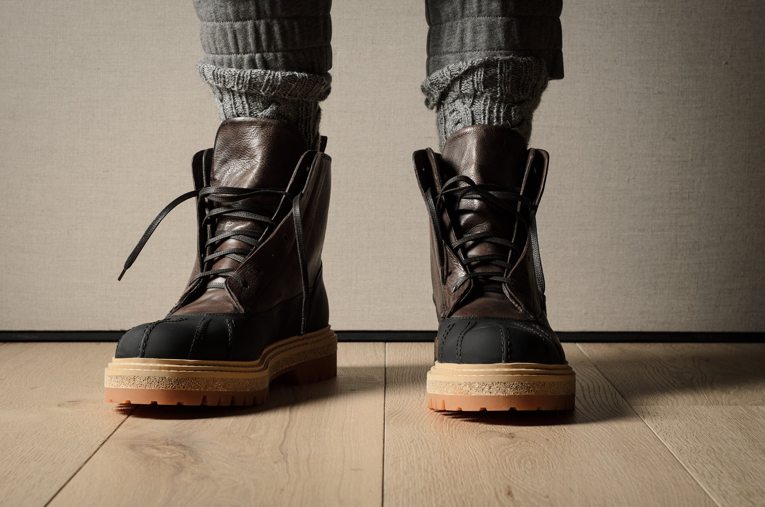 Brown leather hiking boots with tan soles worn by a person on a wooden floor.