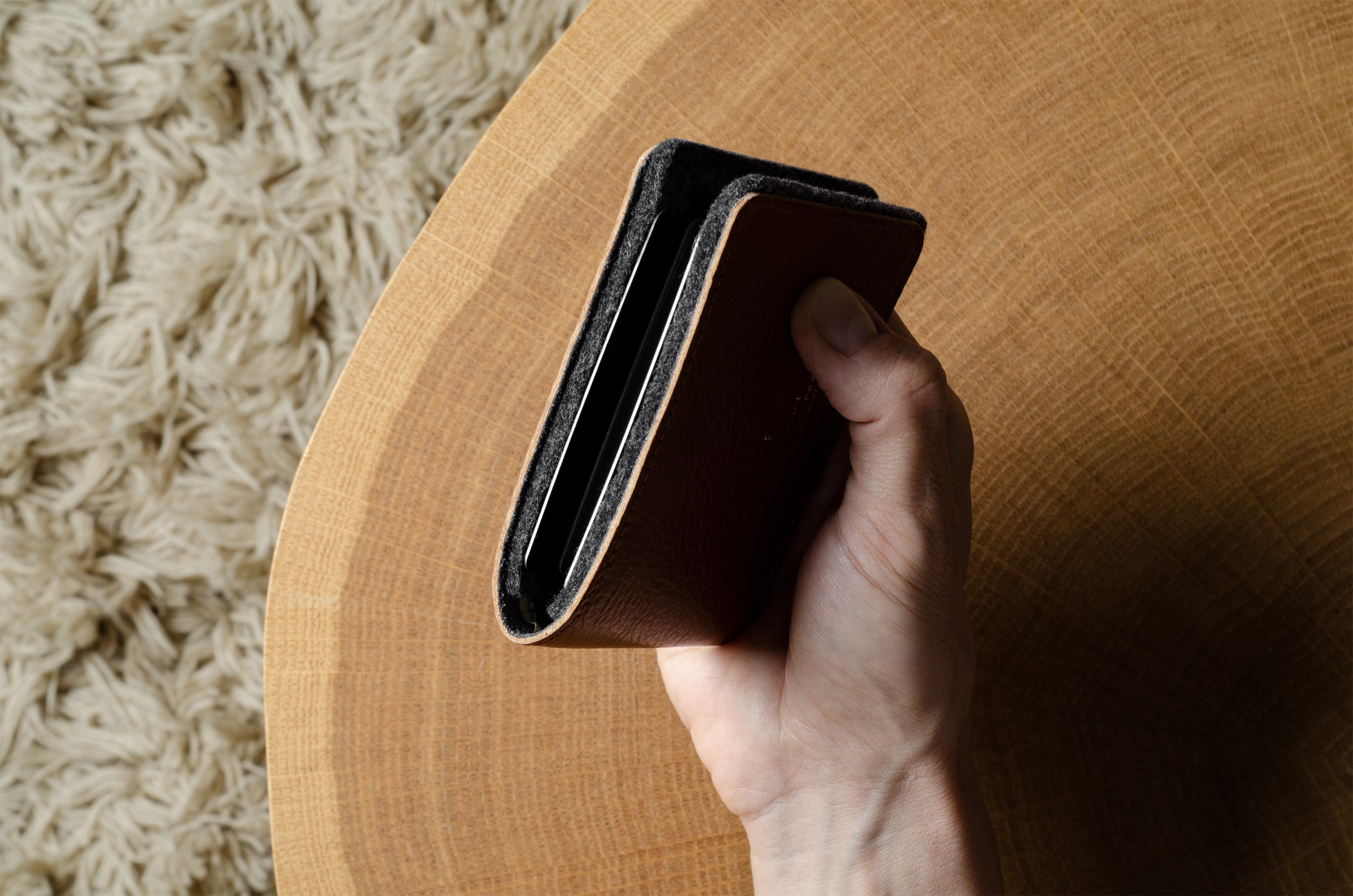 Hand holding a black bi-fold wallet over a wooden surface with a textured beige rug in the background