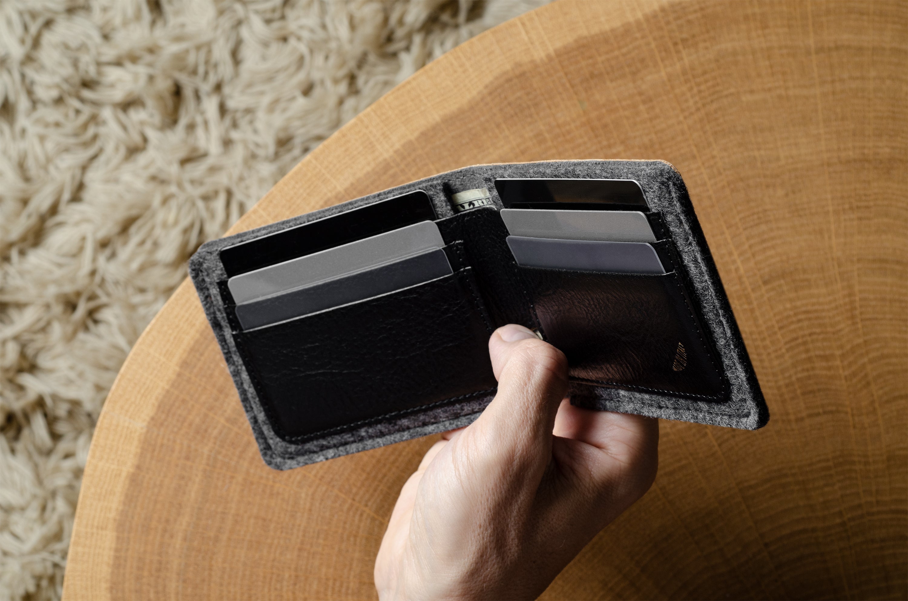 Hand holding an open bi-fold wallet  with cards on a wooden surface
