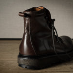 Brown leather boot on a wooden surface with a neutral background