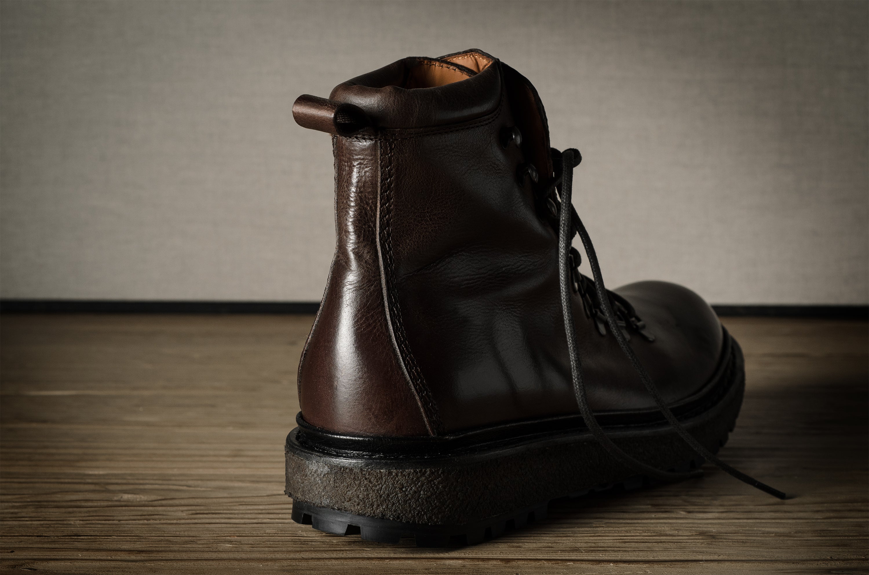Brown leather boot on a wooden surface with a neutral background