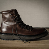 Brown leather boot with black sole on a wooden surface