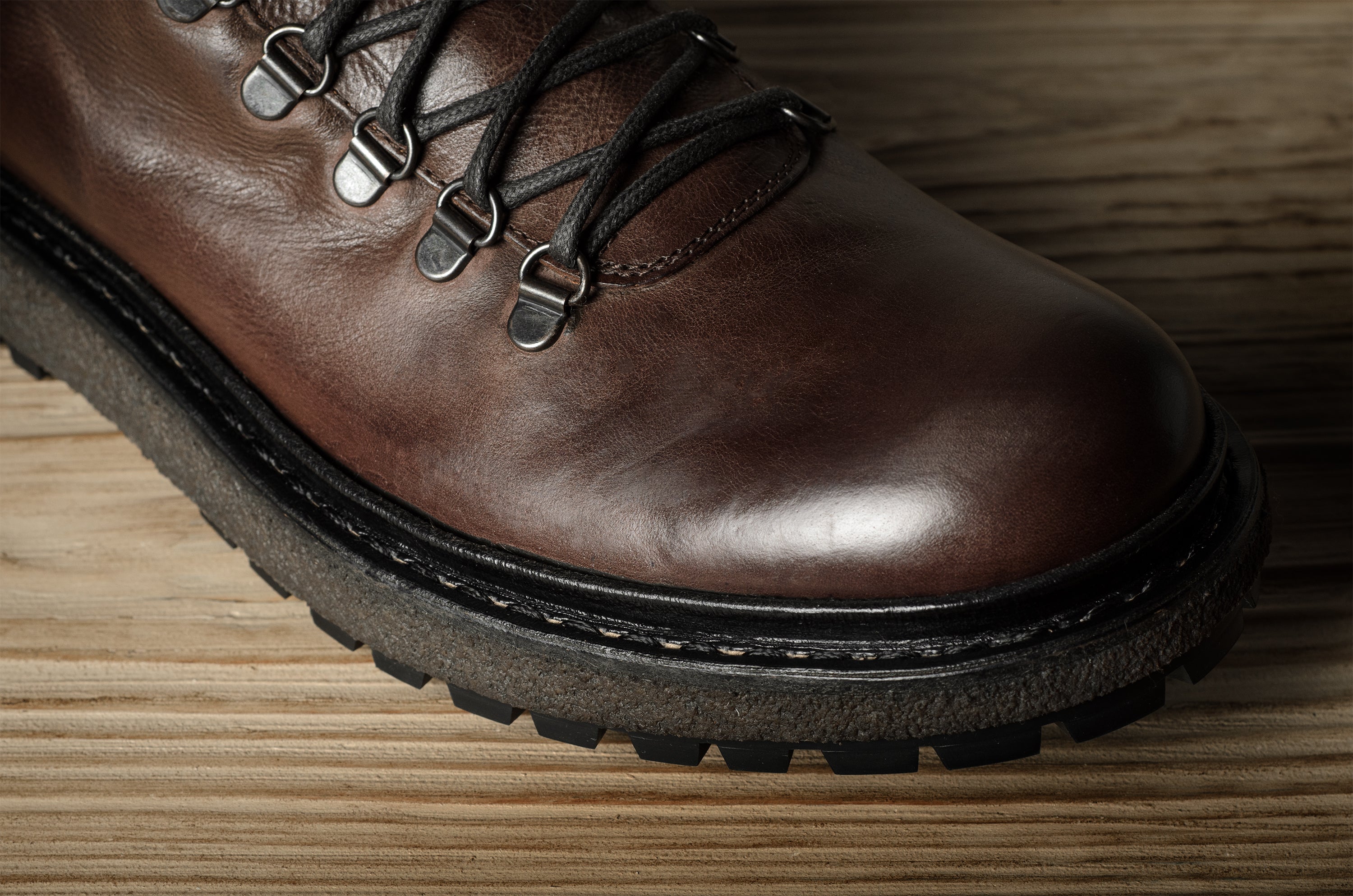 Brown leather boot with black laces on a wooden surface