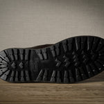 Close-up of a black boot sole on a wooden floor with a neutral wall background
