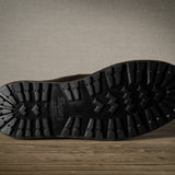 Close-up of a black boot sole on a wooden floor with a neutral wall background
