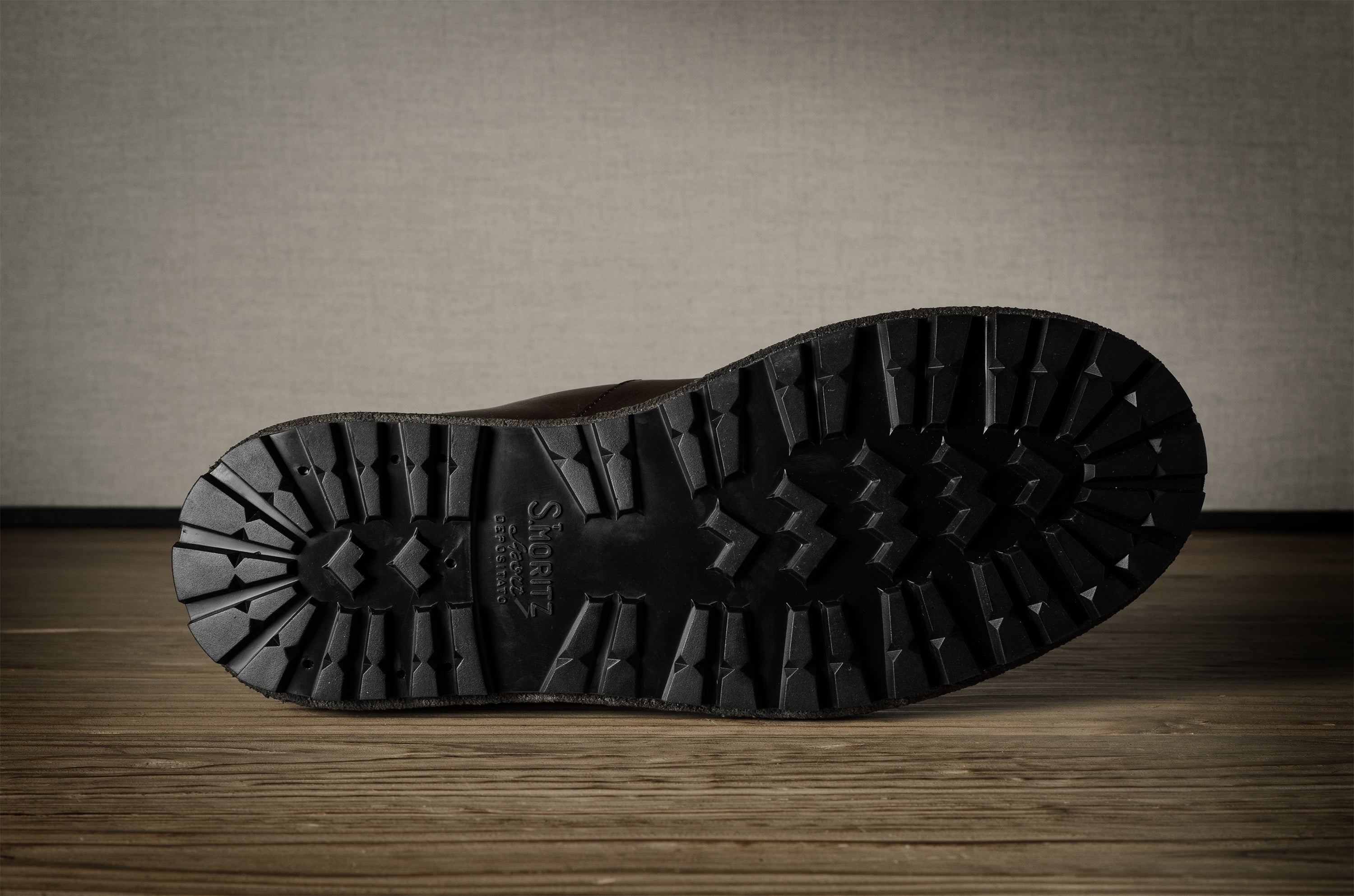 Close-up of a black boot sole on a wooden floor with a neutral wall background