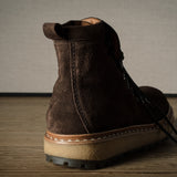 Brown suede boot on a wooden floor with a neutral background