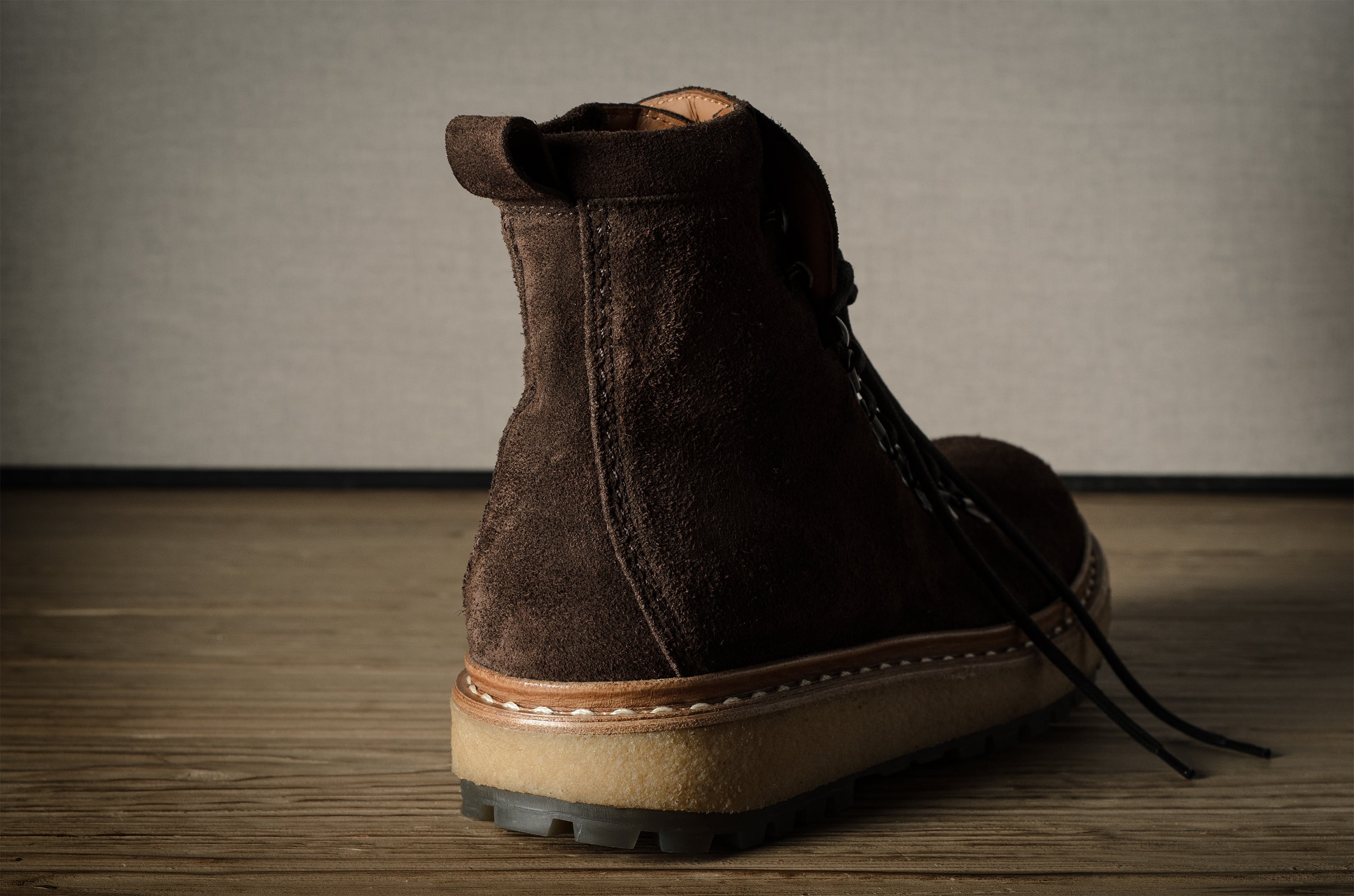 Brown suede boot on a wooden floor with a neutral background