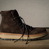 Brown leather boot with a beige sole on a wooden floor