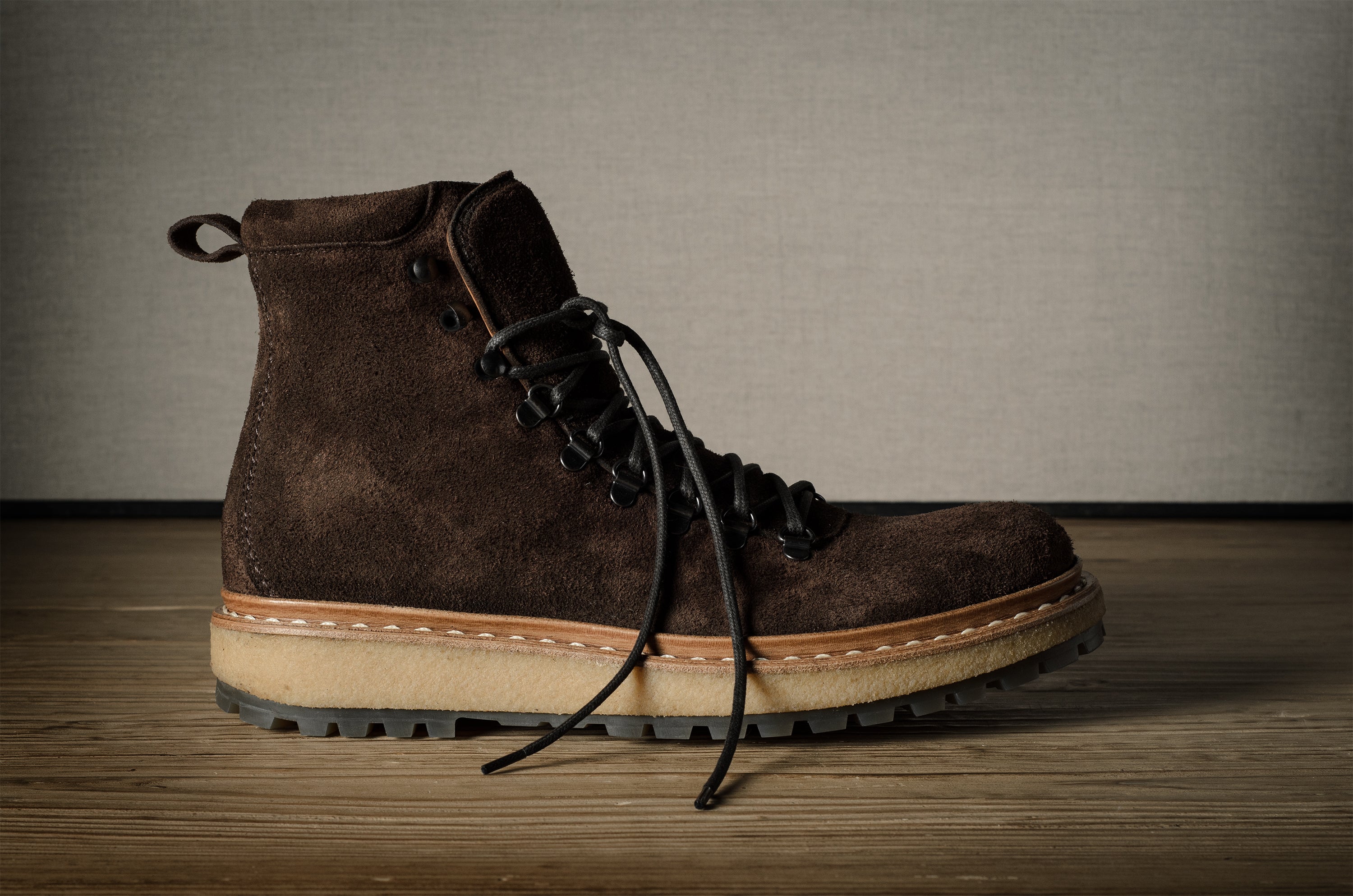 Brown leather boot with a beige sole on a wooden floor