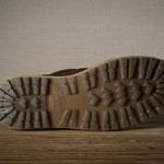 Close-up of a brown boot sole with tread pattern on a wooden floor.