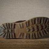Close-up of a brown boot sole with tread pattern on a wooden floor.