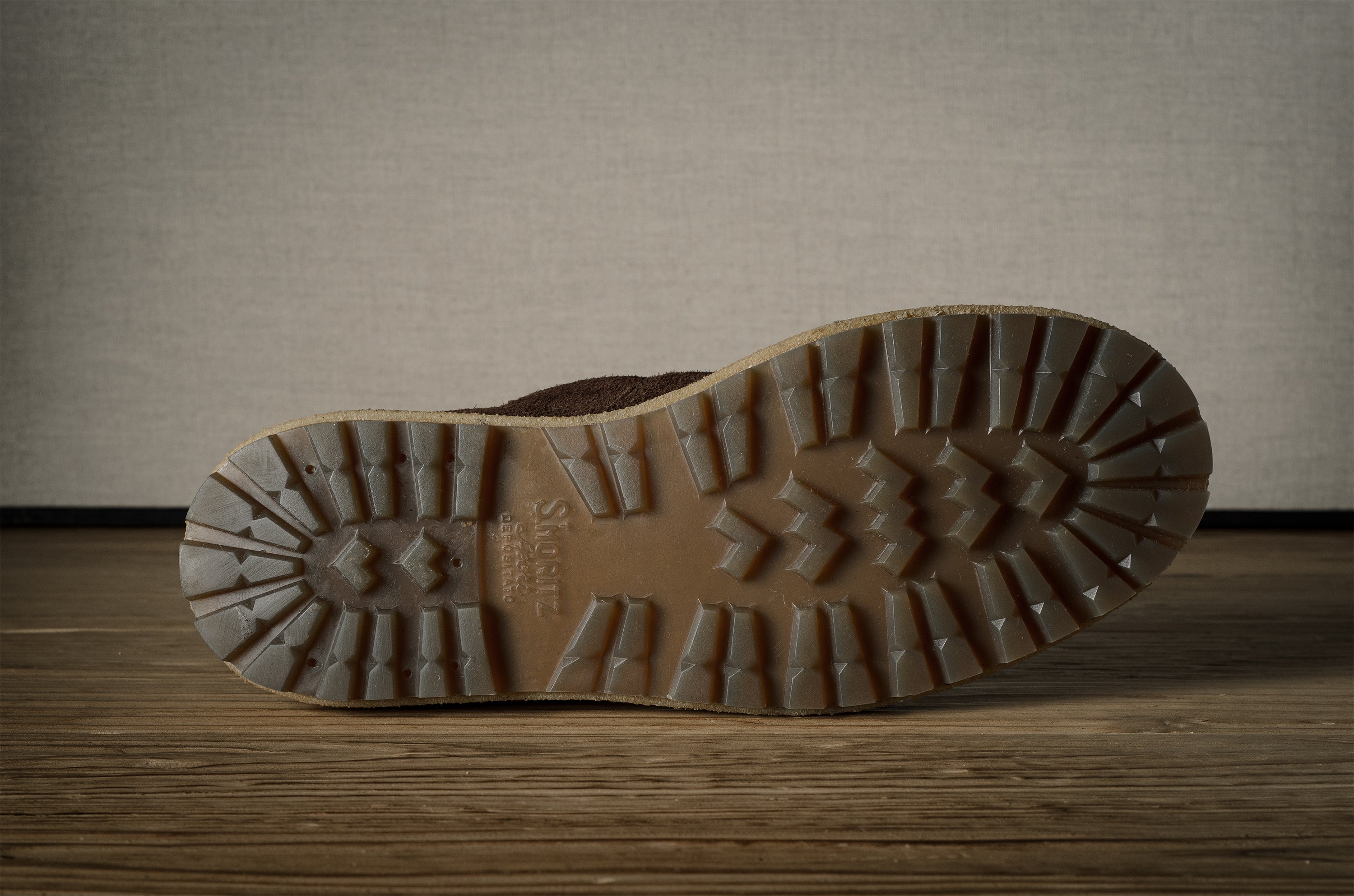 Close-up of a brown boot sole with tread pattern on a wooden floor.