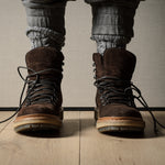 Brown leather boots worn with rolled-up jeans on a wooden floor.
