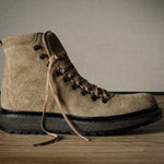 Brown suede boot with black sole on a wooden surface and gray background