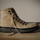 Brown suede boot with black sole on a wooden surface and gray background