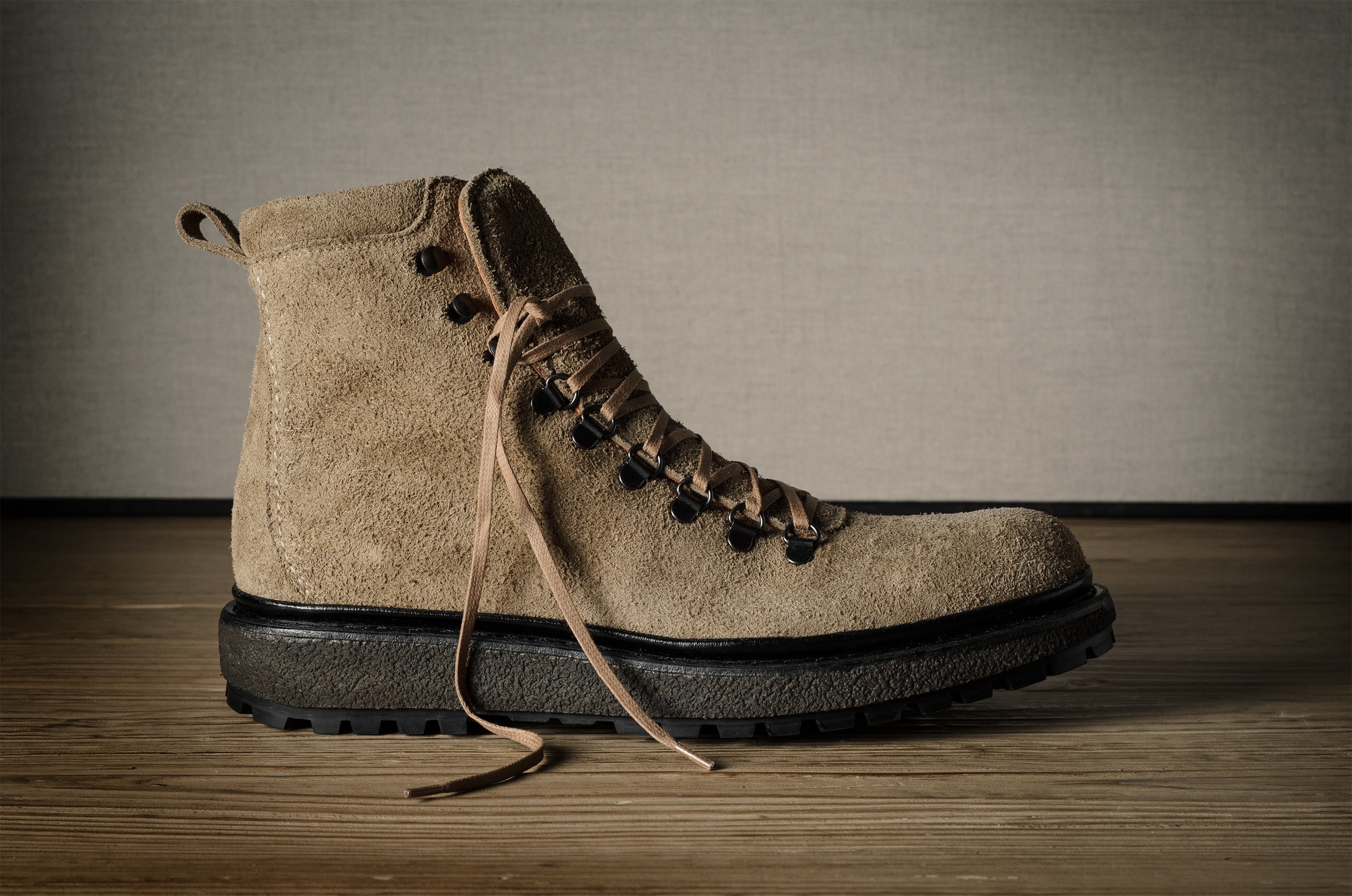Brown suede boot with black sole on a wooden surface and gray background