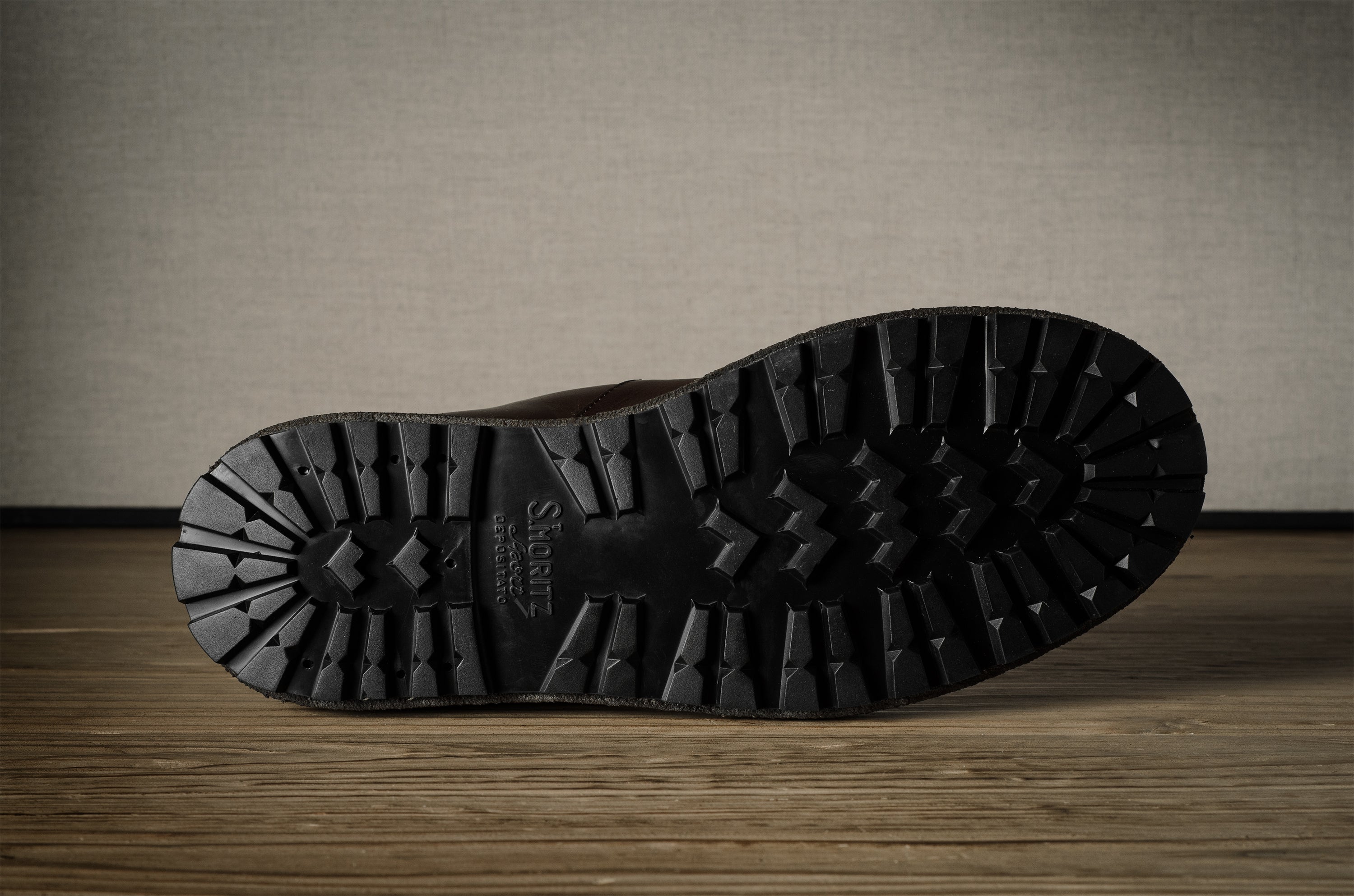 Close-up of a black boot sole with brand logo on a wooden surface.