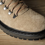 Close-up of a brown suede boot with a black sole on a wooden surface