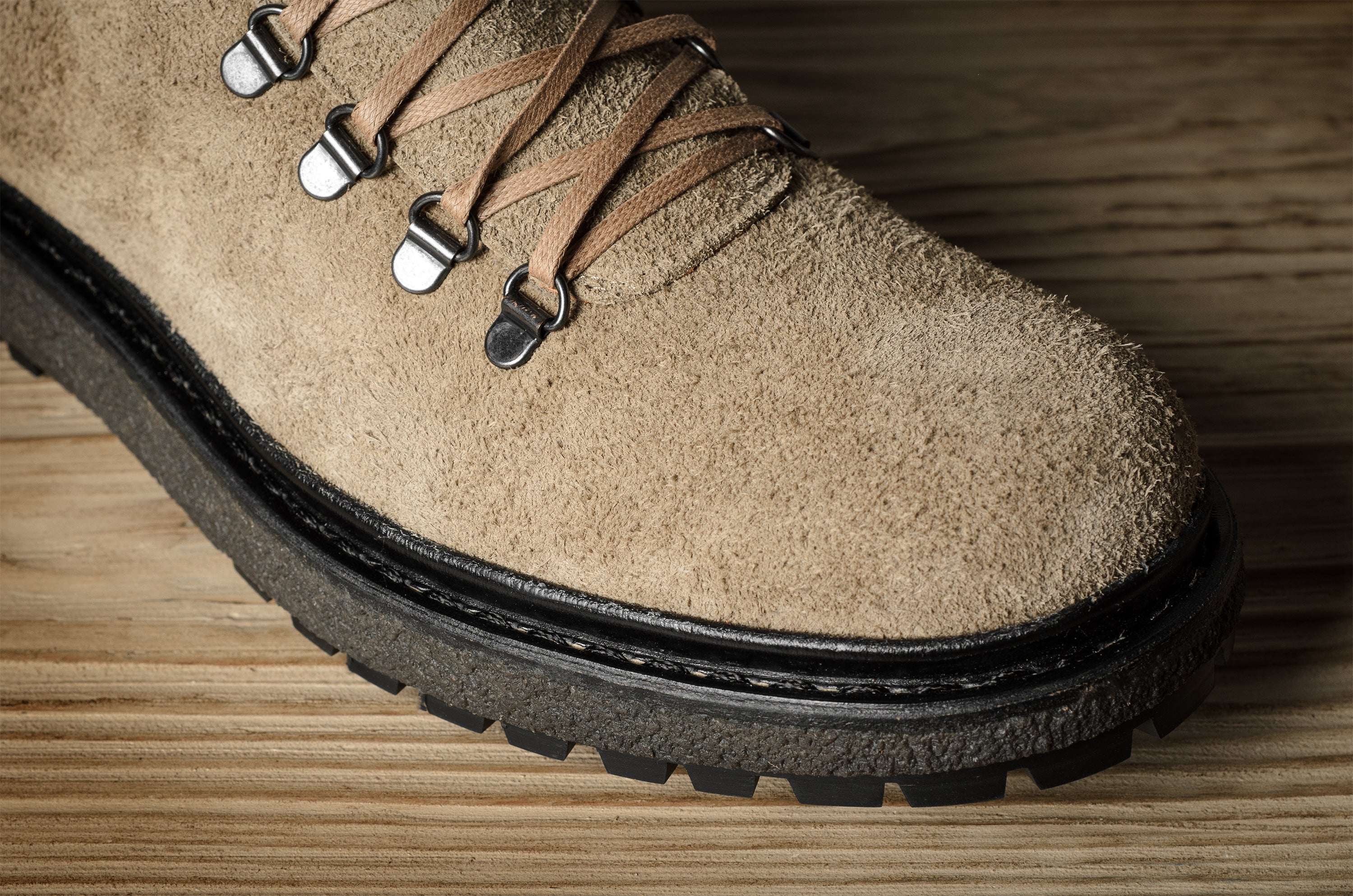 Close-up of a brown suede boot with a black sole on a wooden surface