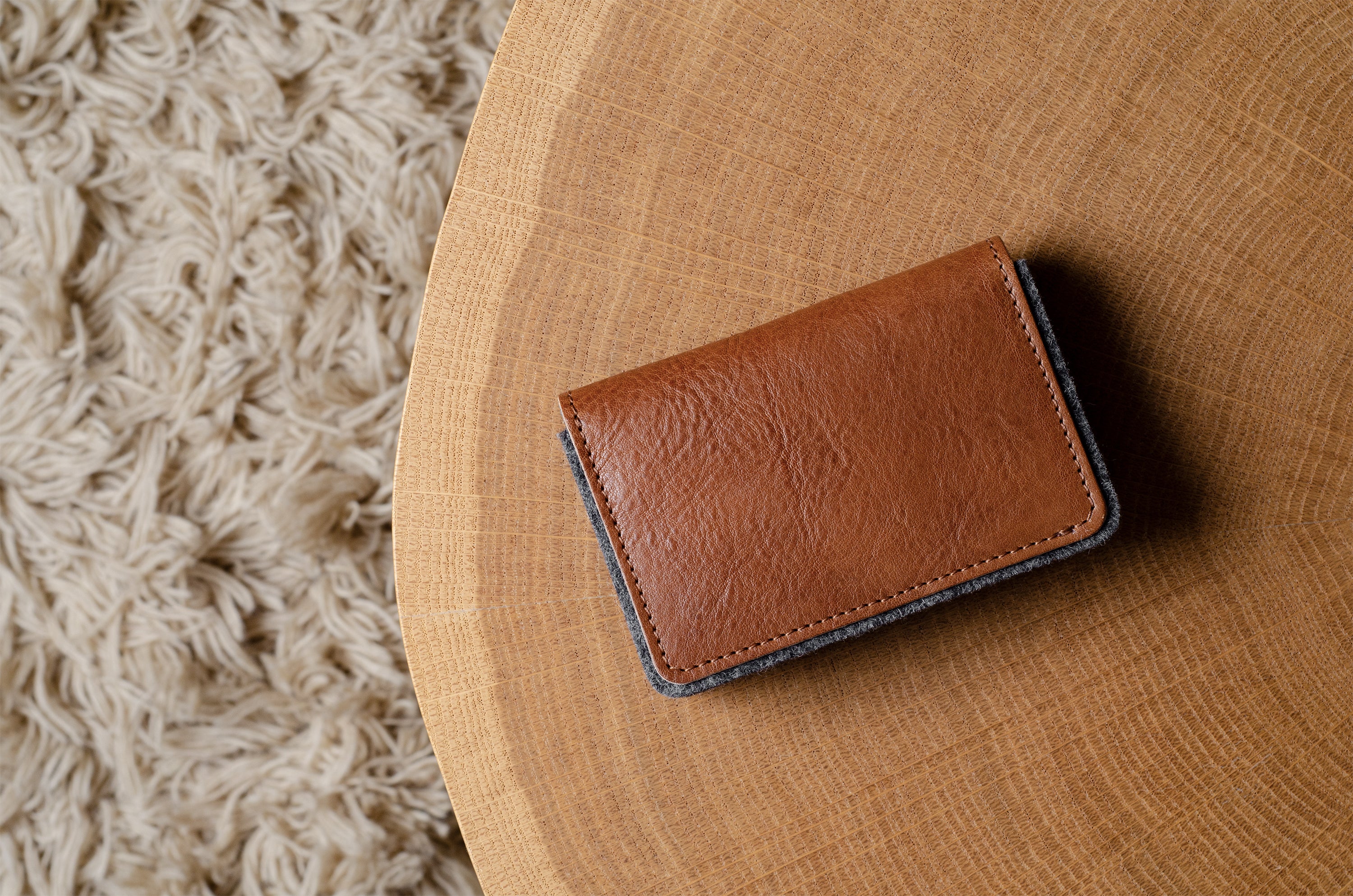 Brown leather wallet on a wooden surface with a textured rug in the background