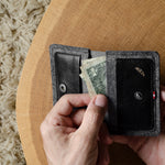 Person holding a black wallet with money on a wooden surface