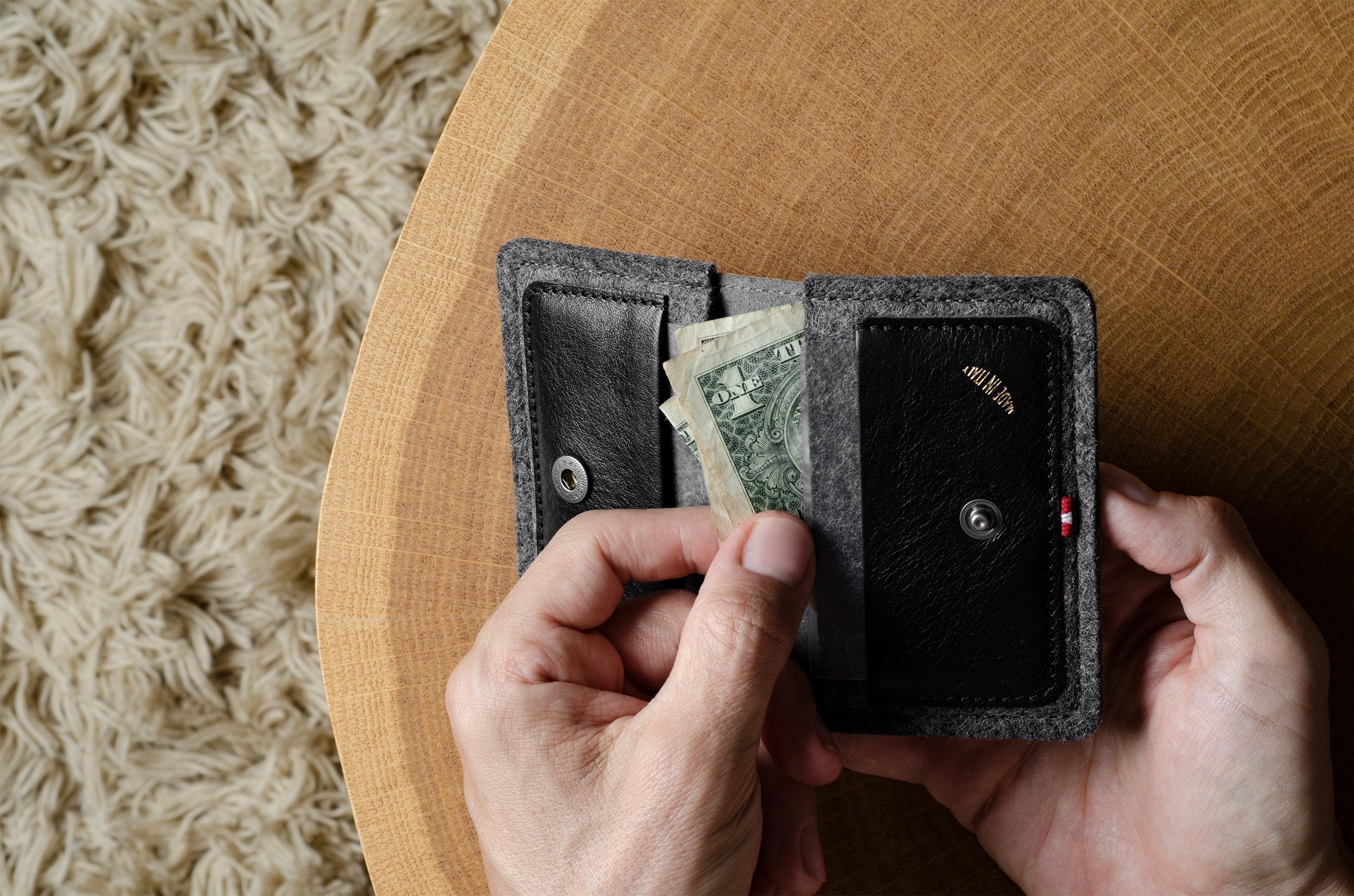 Person holding a black wallet with money on a wooden surface