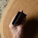 Hand holding a wallet on a wooden surface with a textured beige rug in the background
